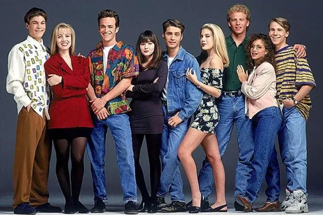 A group of nine smiling young adults in 1990s fashion, showcasing various styles of denim, patterns, and casual wear.