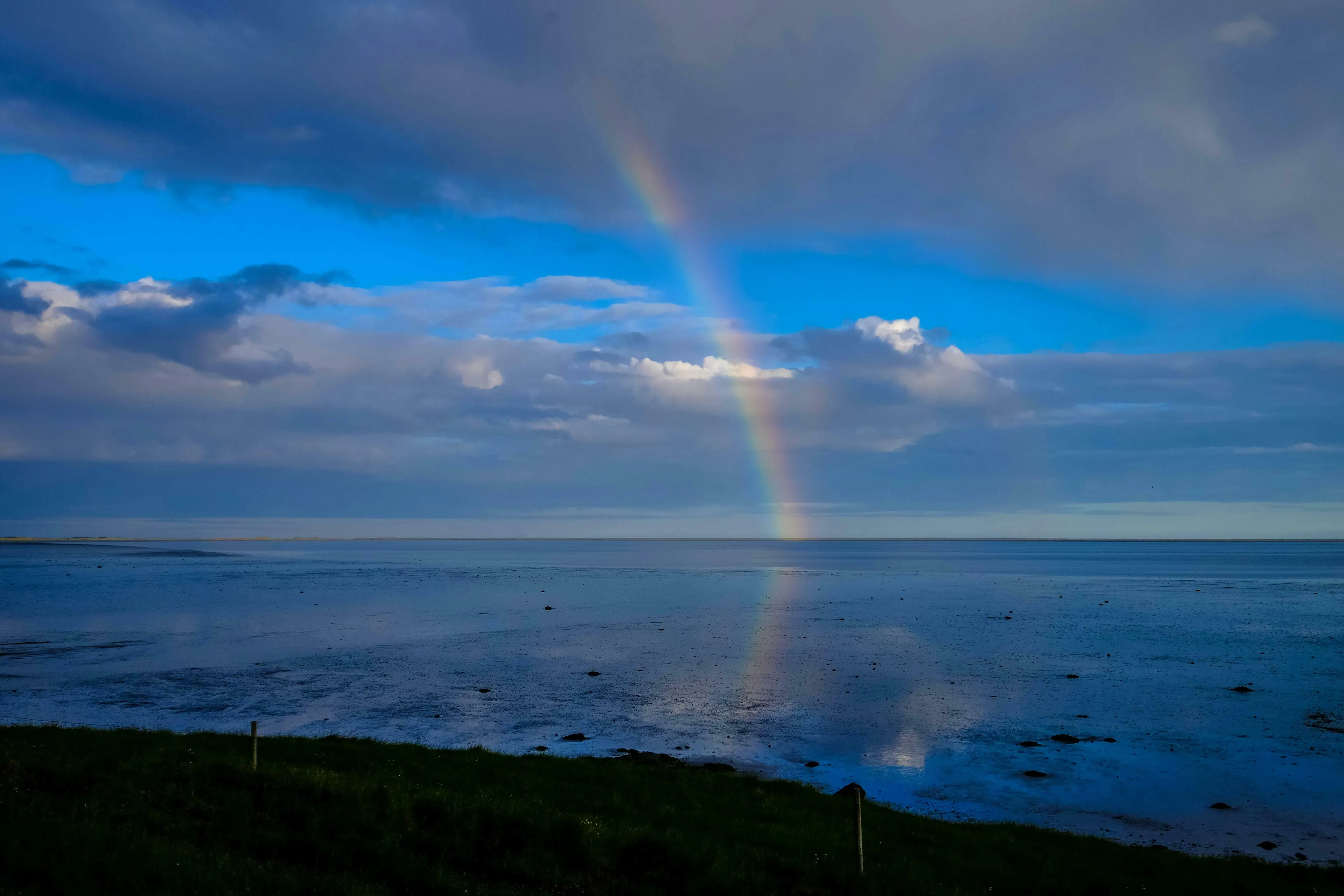 A vivid rainbow arches over a calm ocean under a partly cloudy sky. The Who Wants To Be A Millionaire question asks about colors.