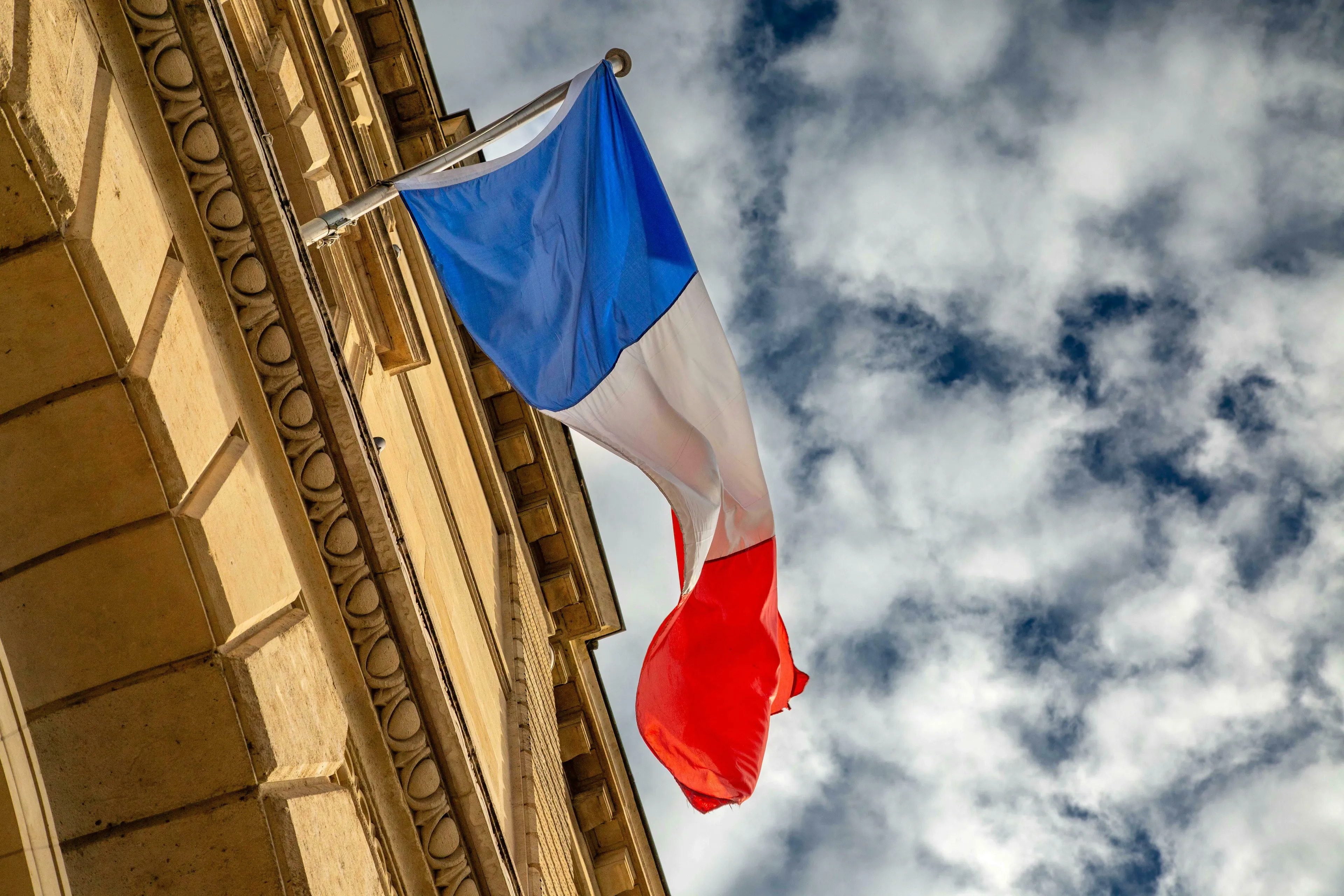 French flag flying from a building, with a cloudy sky backdrop. Who Wants to Be A Millionaire question on France.