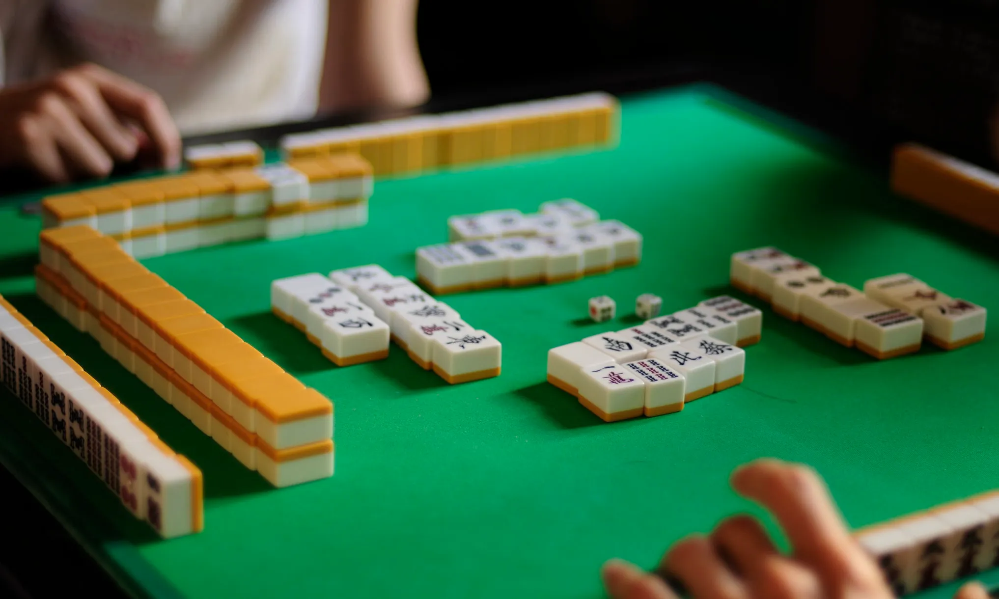 Players gathered around a green table, hands reaching for Mahjong tiles, immersed in this game called Mahjong.