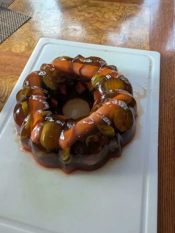 A savory gelatin ring with hot dogs and pickles as a questionable food combo served on a board.