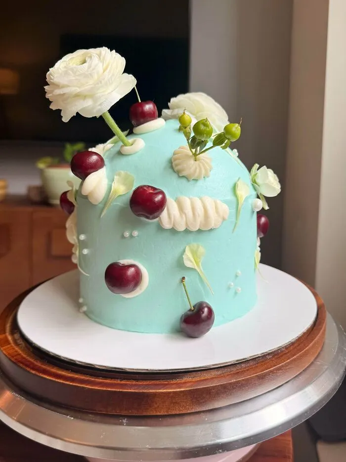 Blue cake adorned with cherries, white flowers, and green berries