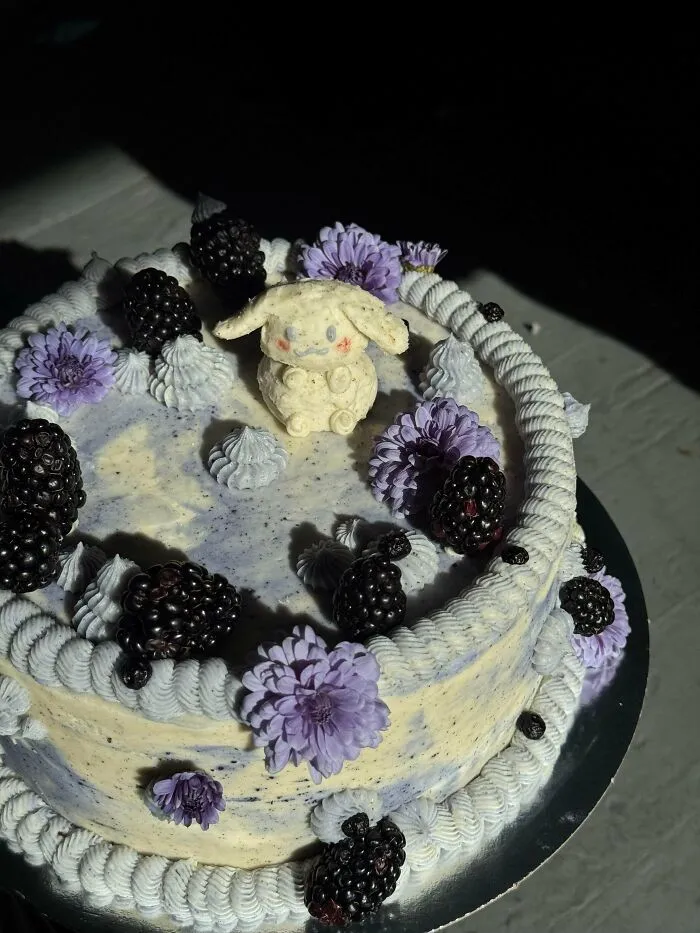 Cake decorated with blackberries, purple flowers, and a fondant animal figure