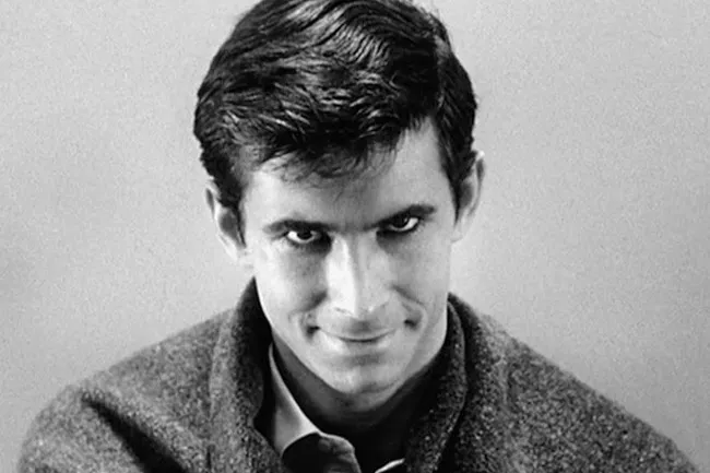 A black and white close-up of Norman Bates from Psycho, smirking ominously, a classic villain.