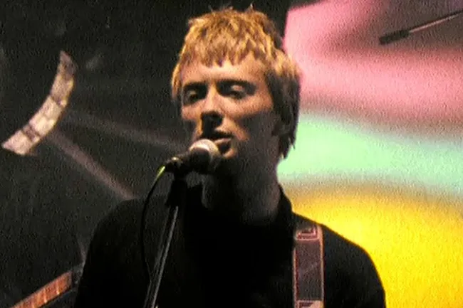 Thom Yorke of Radiohead performing Creep live, with blonde hair and a black shirt, at a concert.