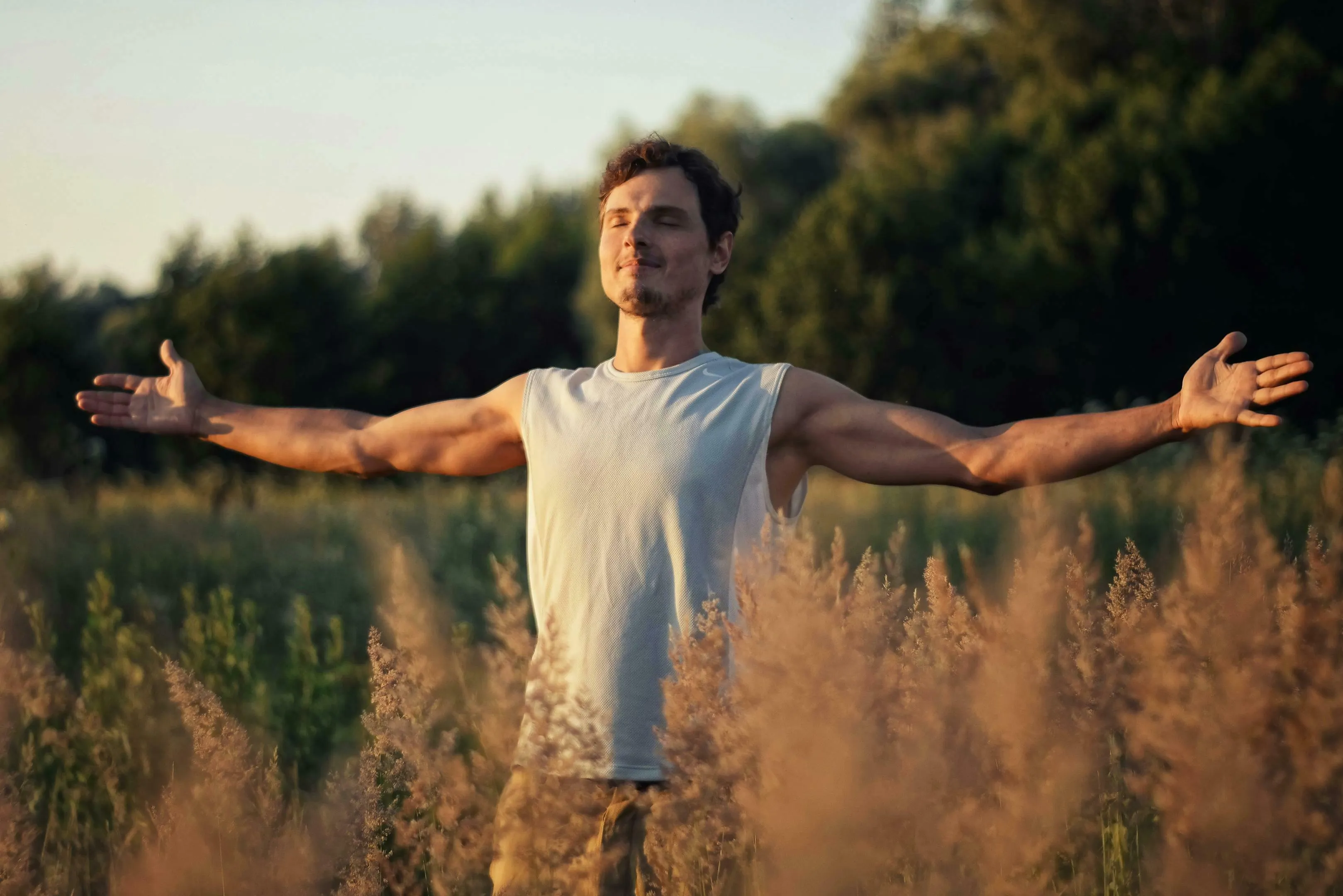 Man breathing in a field of tall grass, arms outstretched, eyes closed in calm. General Knowledge quiz, human respiration.