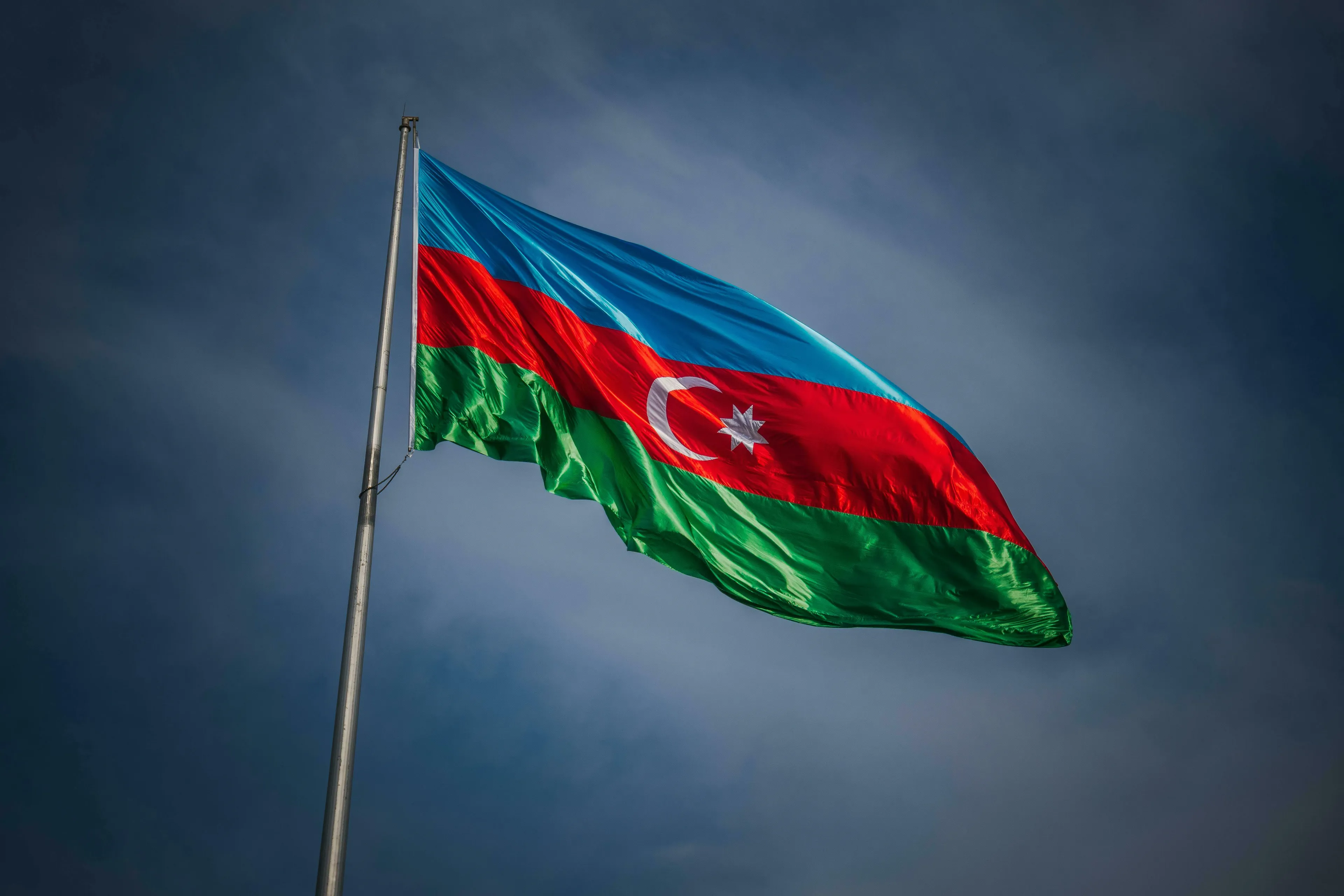 Flag of Azerbaijan fluttering against a cloudy sky, hinting at general knowledge about its capital.