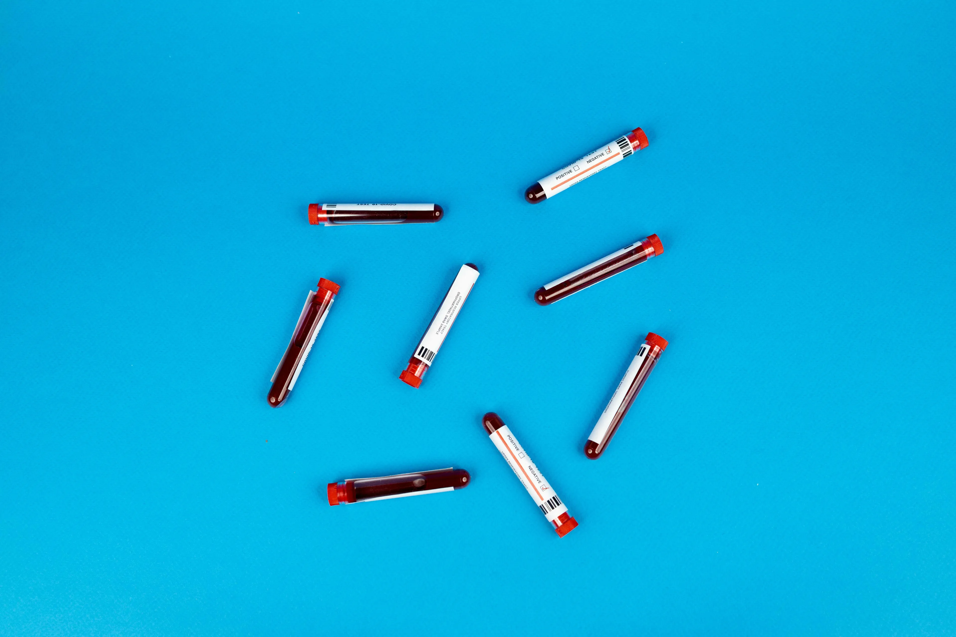 Seven medical blood sample vials on a bright blue background, ready for analysis, a general knowledge quiz on universal plasma donor.