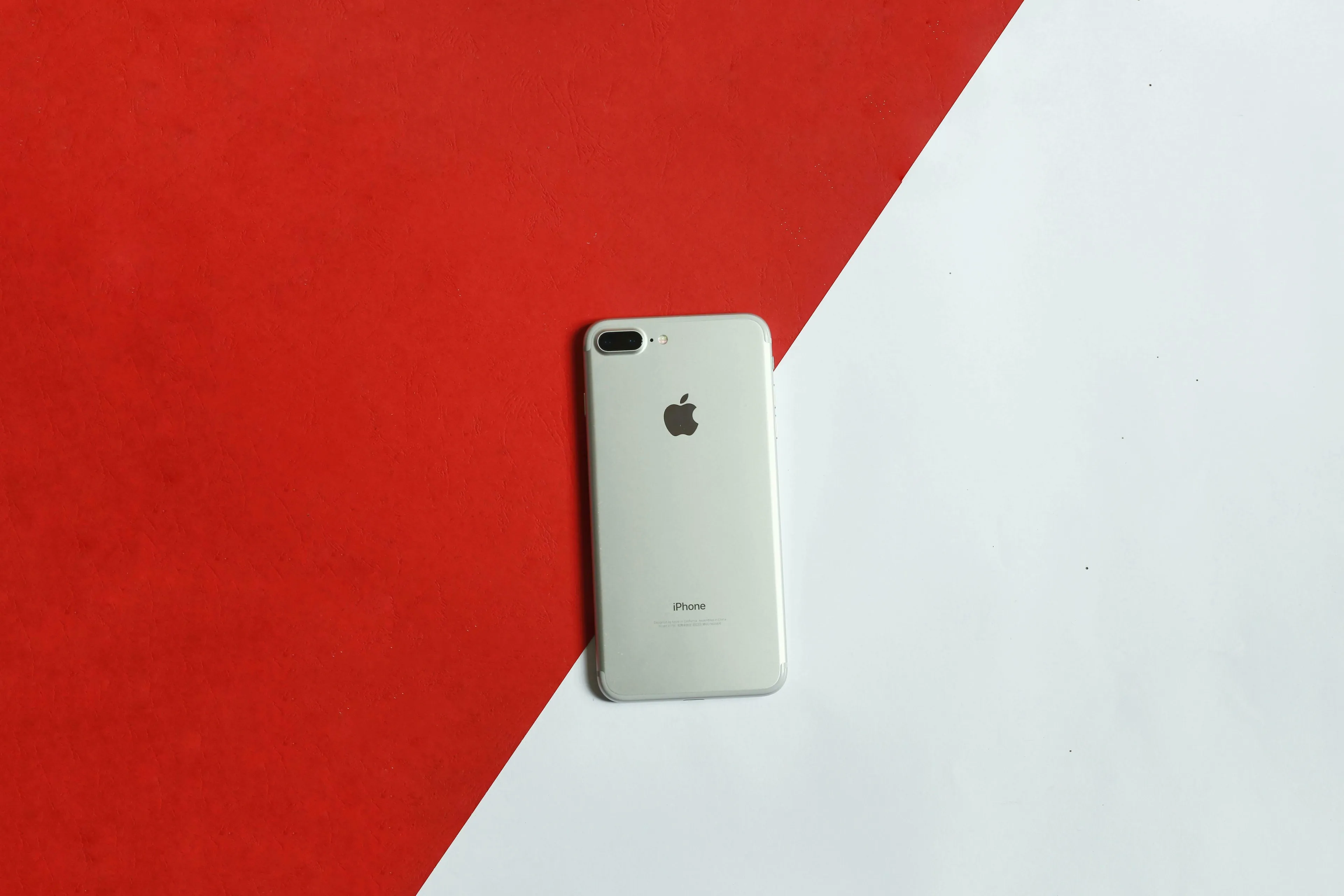 Back of a silver iPhone on a red and white diagonal background. General Knowledge Quiz: What time does the iPhone home screen display?