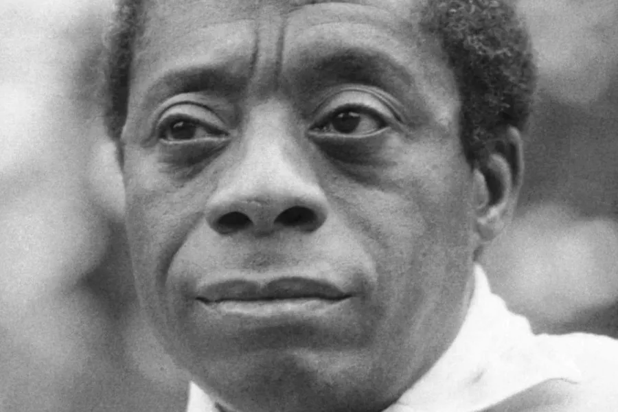 Close-up black and white photo of James Baldwin, a serious expression on his face, looking slightly upward.