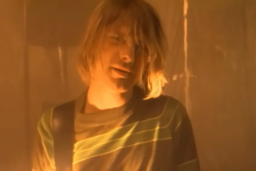 Kurt Cobain, Nirvana's lead singer, in a warm-toned, hazy close-up, wearing a striped shirt.