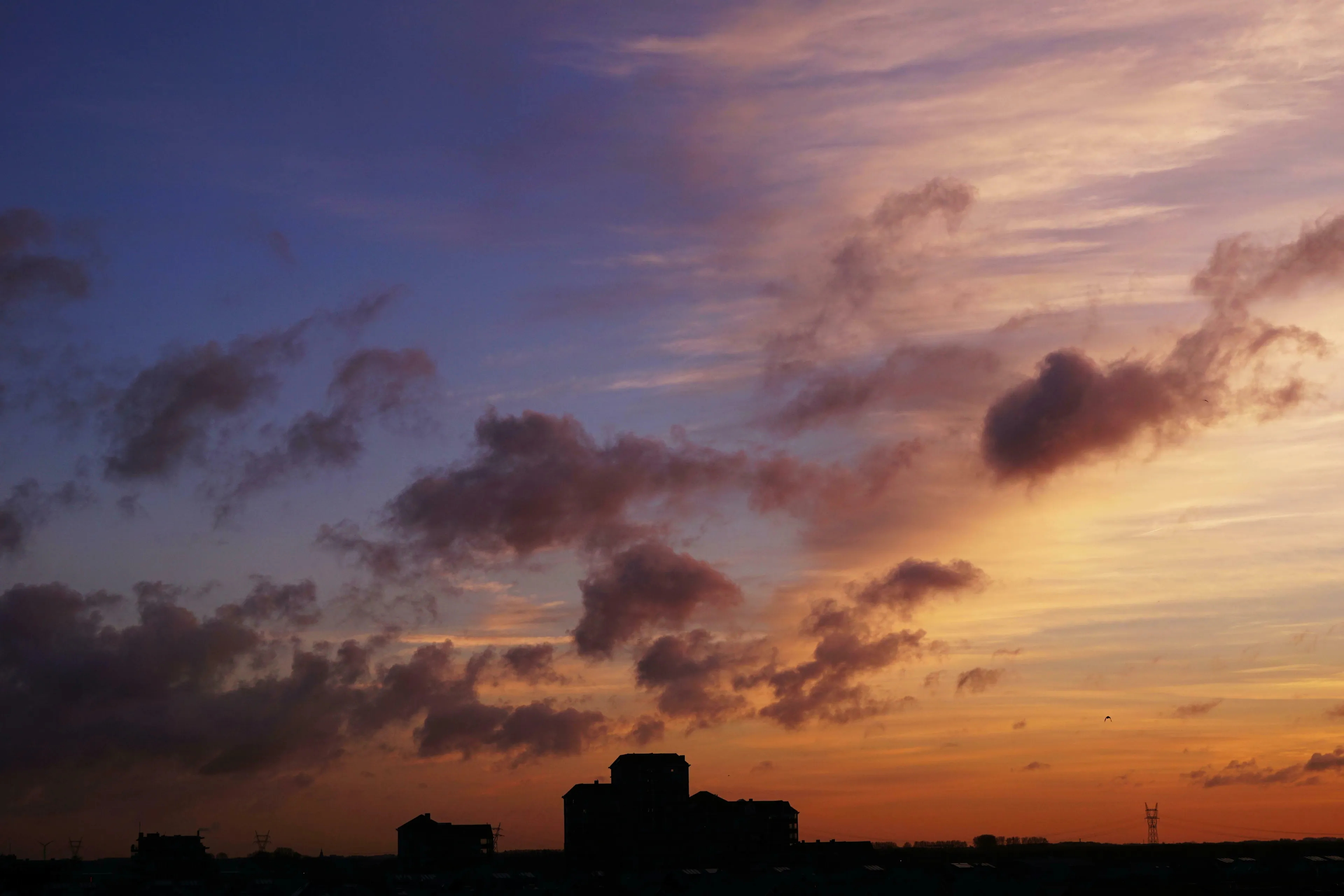 A dramatic procrastination type sunset with purple and orange hues over a dark cityscape, illustrating twilight's approach.