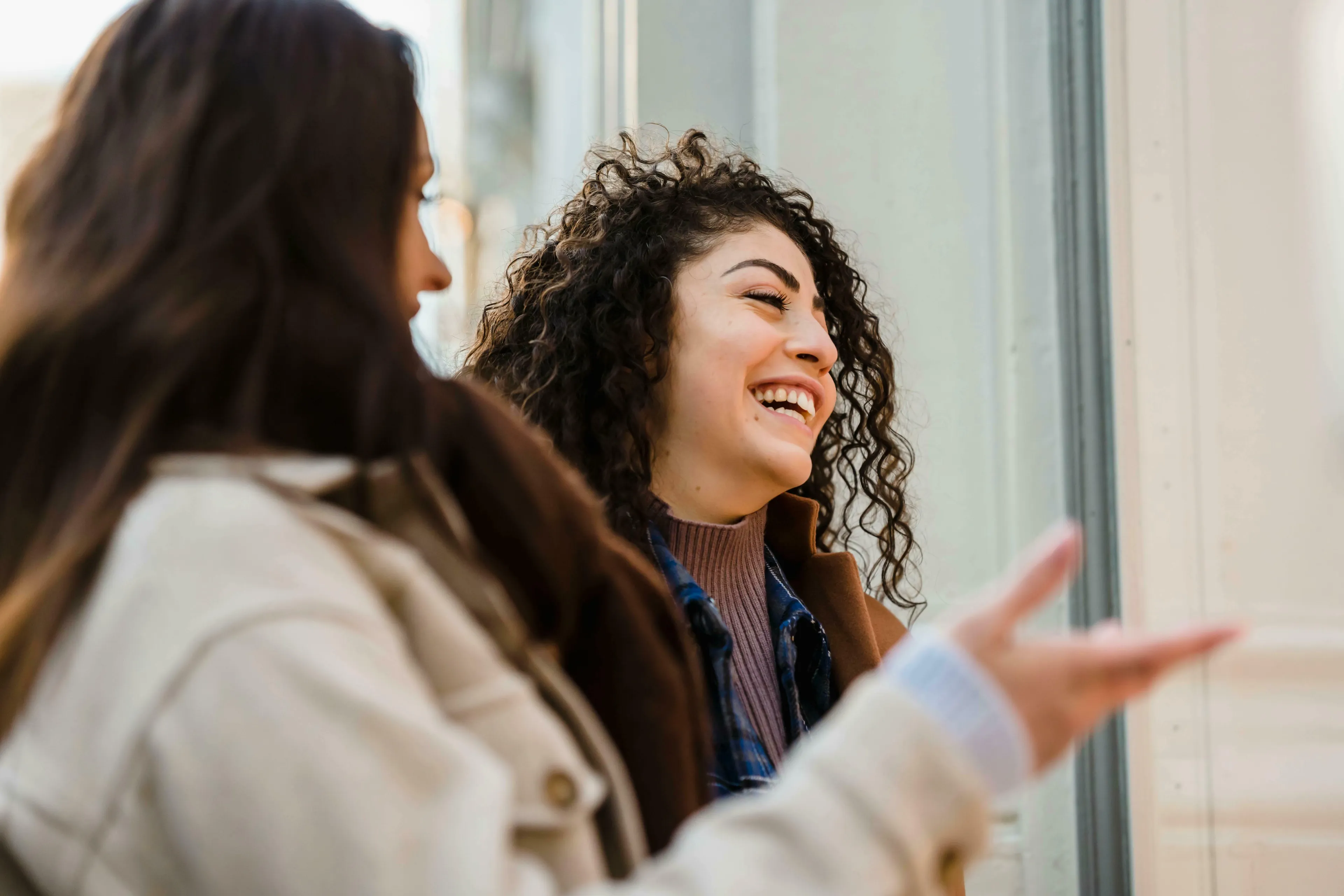 Two friends talking; one with curly hair laughs. What's your procrastination type? Your friend describes you...
