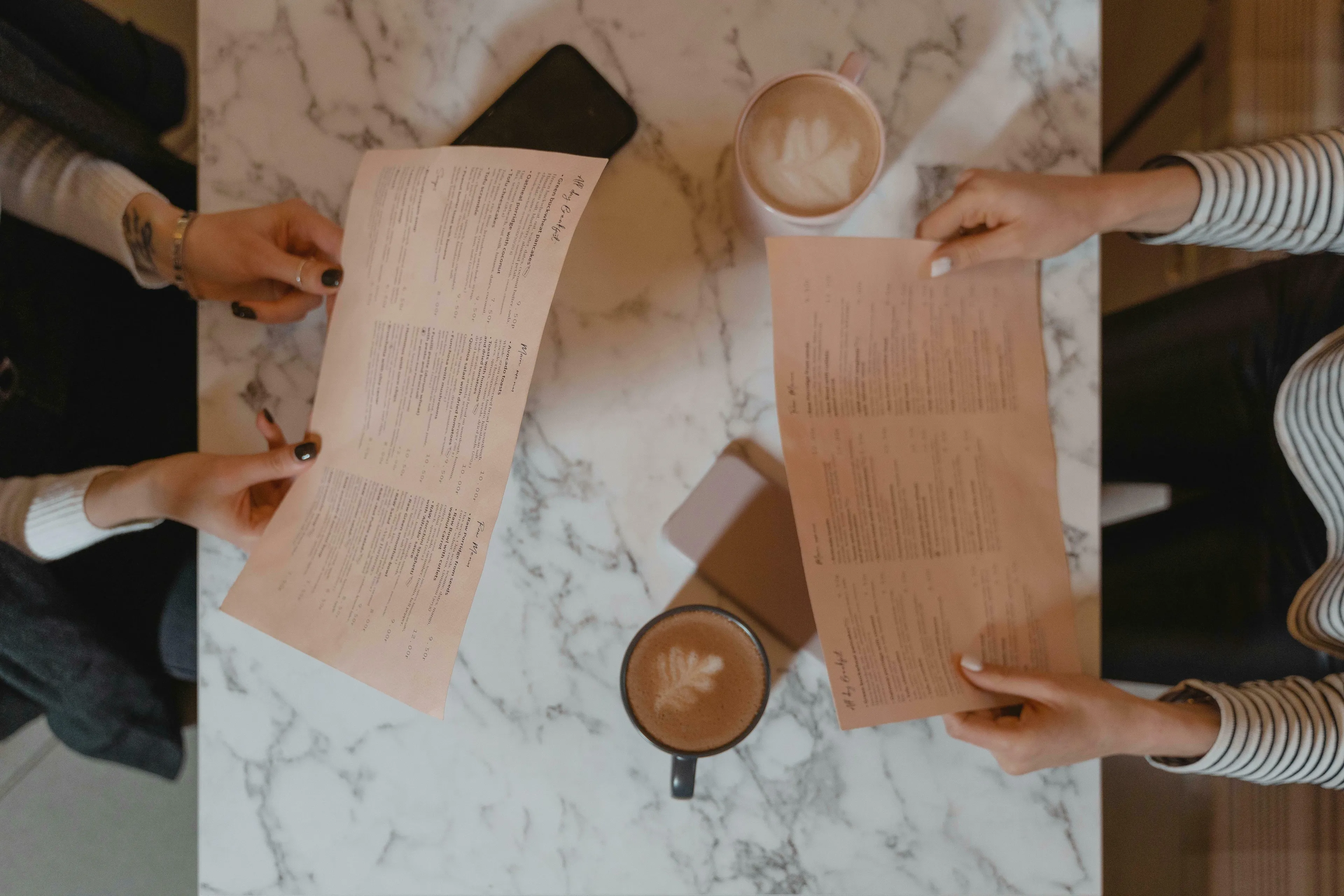 Two people at a marble table holding restaurant menus, with coffee cups, facing a procrastination type decision.