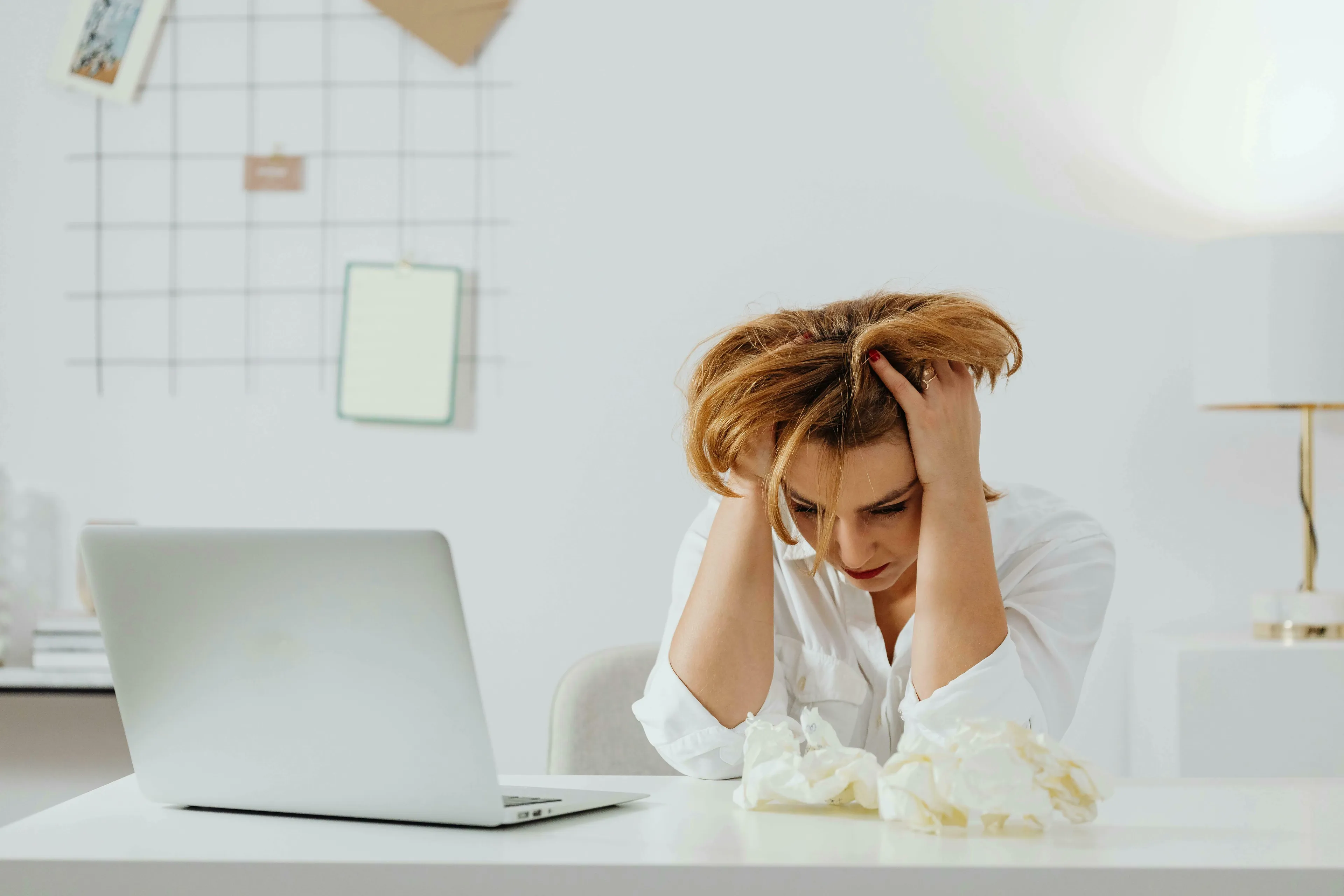 A stressed woman with hands in her hair, surrounded by crumpled paper, showing what's your procrastination type when overwhelmed.