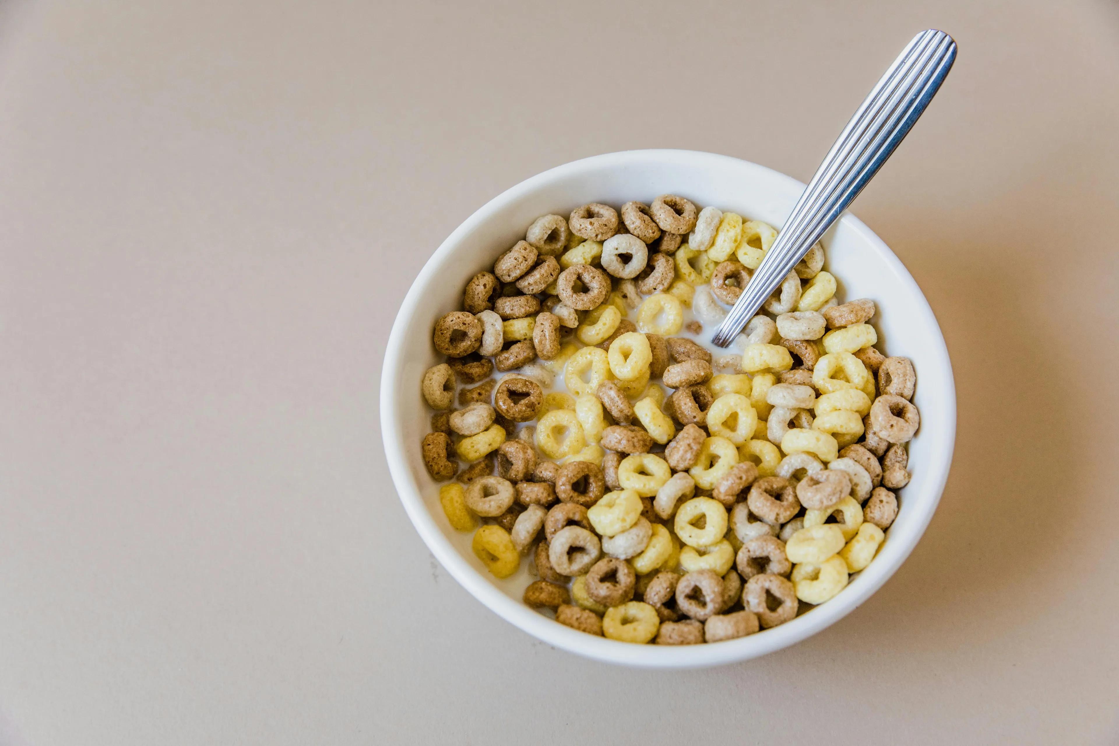 A white bowl filled with ring-shaped cereal in two colors, light yellow and brown, with milk and a spoon.
