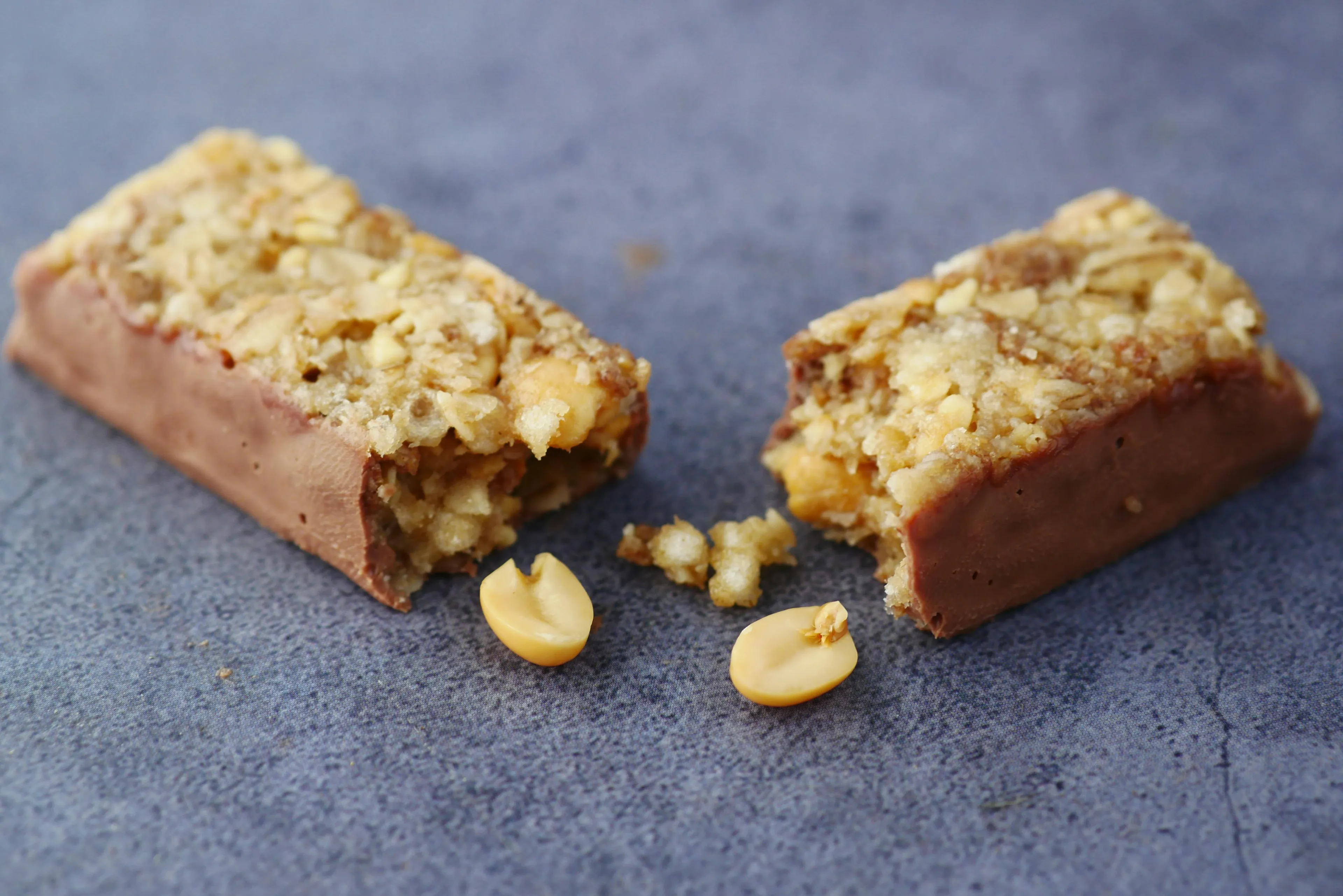 A broken granola bar with peanuts on a gray surface, a great snack to match your working style.