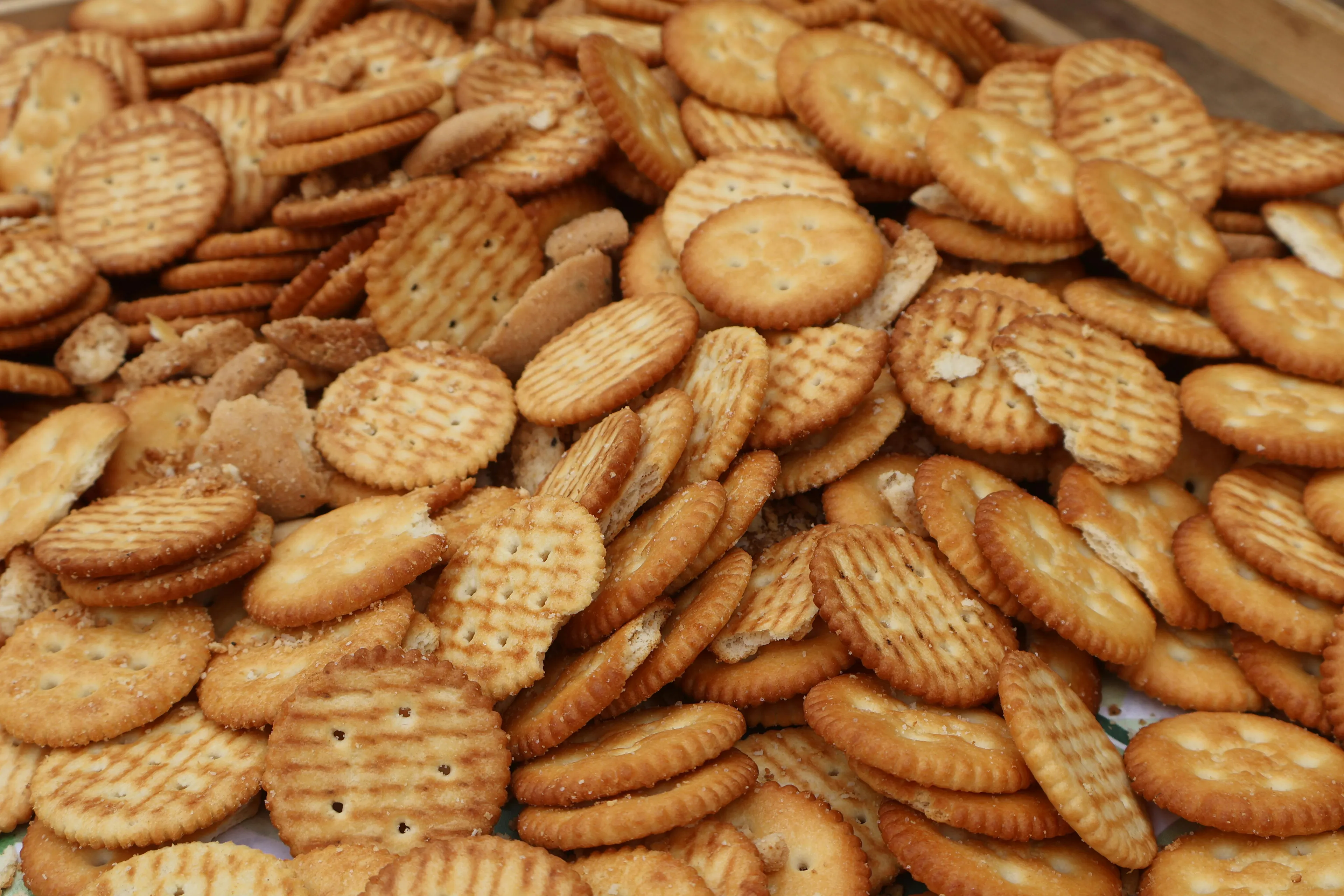 A close-up of a pile of golden-brown crackers with various shapes and textures, some sprinkled with salt.