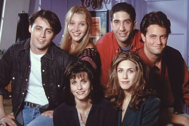 The main cast of the TV show Friends, smiling and posing together. Joey, Phoebe, Ross, Chandler, Monica, and Rachel.