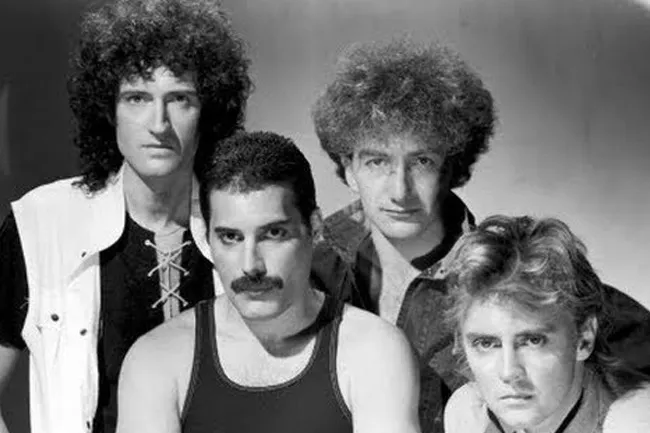 Black and white photo of the band Queen, featuring Freddie Mercury in a tank top. Procrastination theme song, Under Pressure.