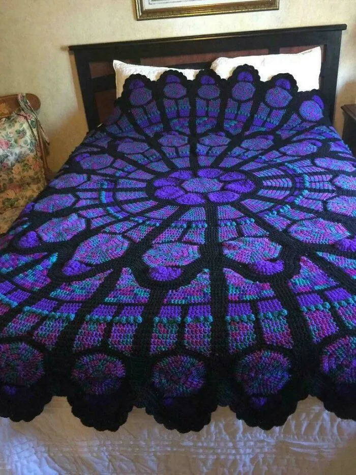 Purple and black crocheted blanket with stained glass window design on bed
