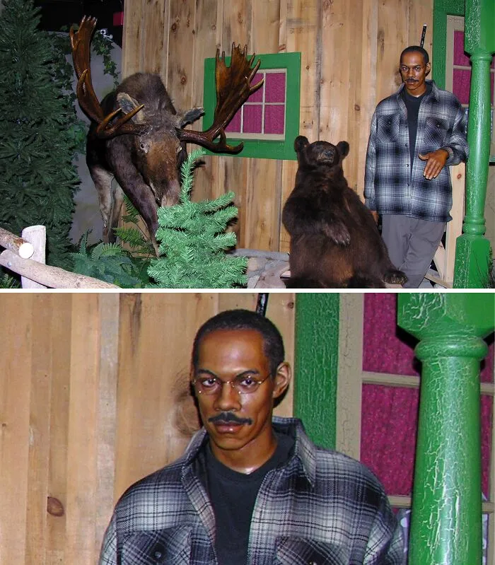 Wax figure of a man standing beside stuffed bear and moose display in rustic setting