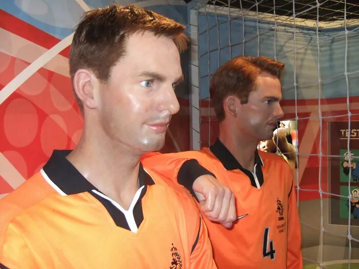 Two male celebrity wax figures in orange sports jerseys near soccer goal