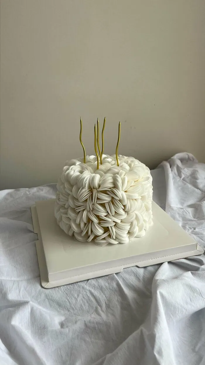 White textured birthday cake with gold candles on a white cloth background