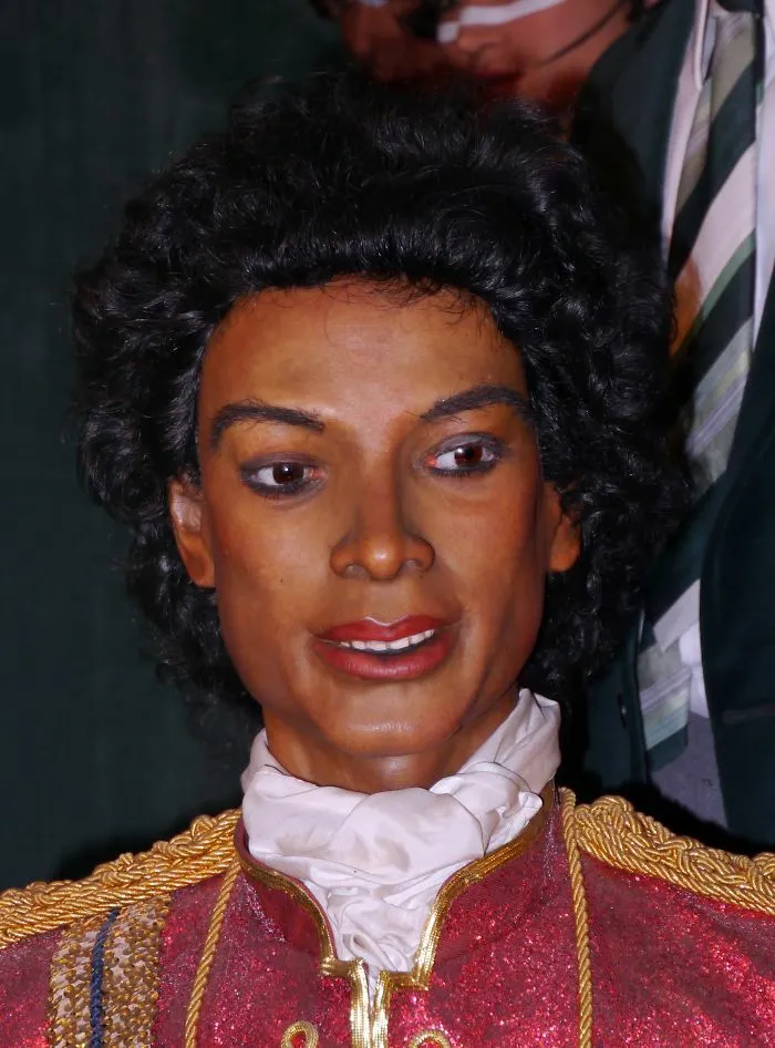 Celebrity wax figure with curly black hair and a red and gold costume with a white collar
