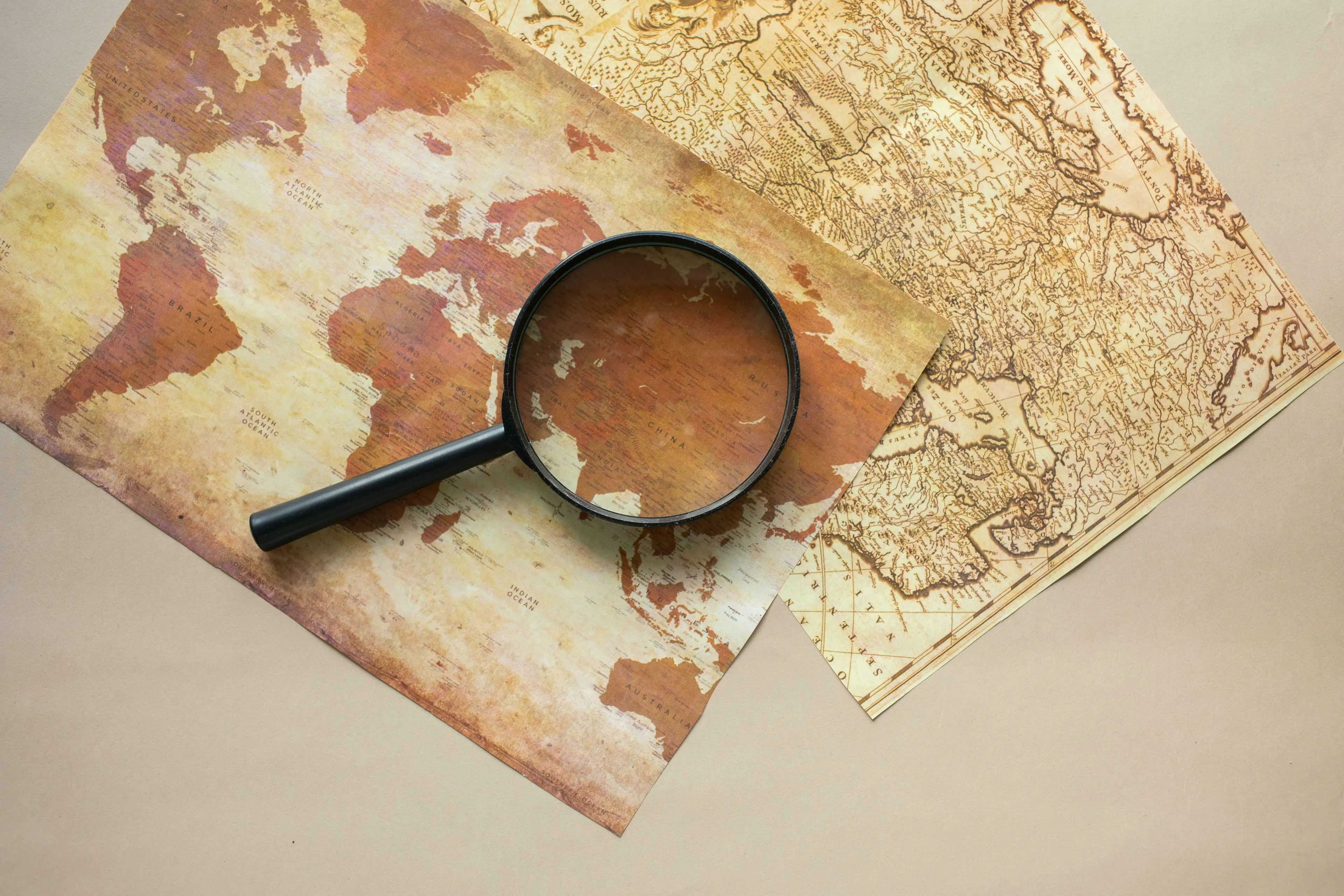 A magnifying glass on antique world maps. Perfect for a general knowledge quiz on the smallest country in the world by area.