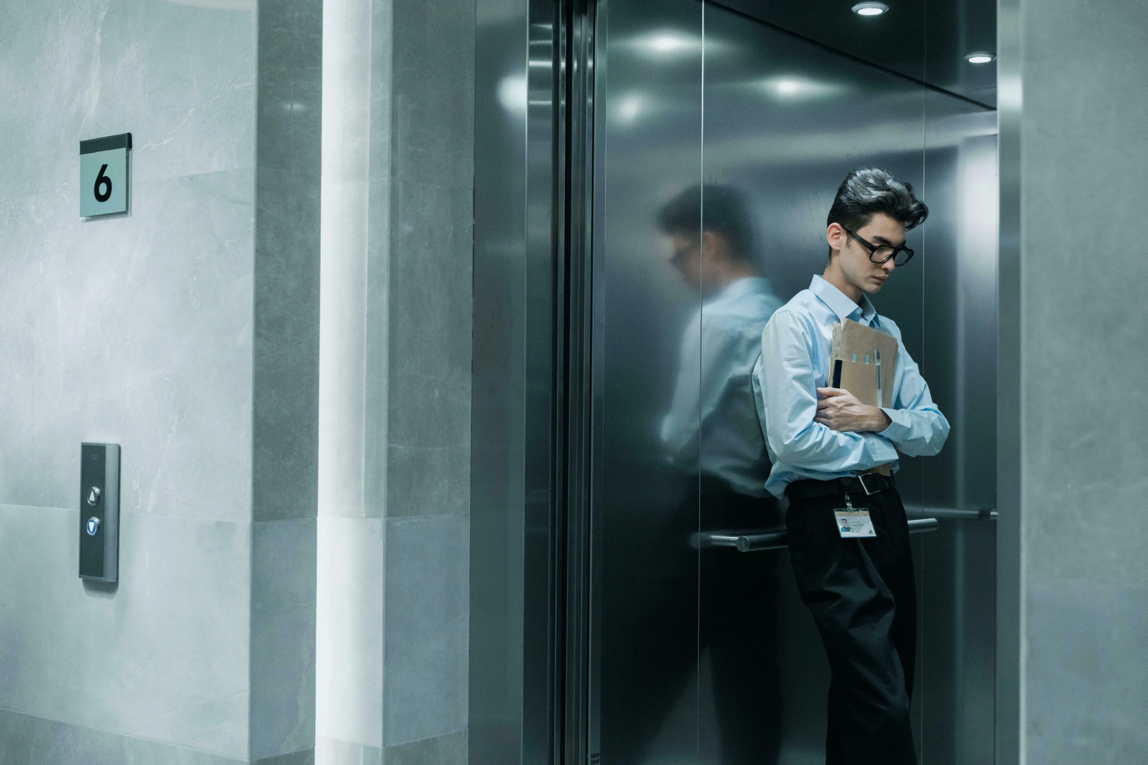 A young man with glasses looks down, visibly anxious inside an elevator. A perfect visual for a General Knowledge Quiz on phobias.