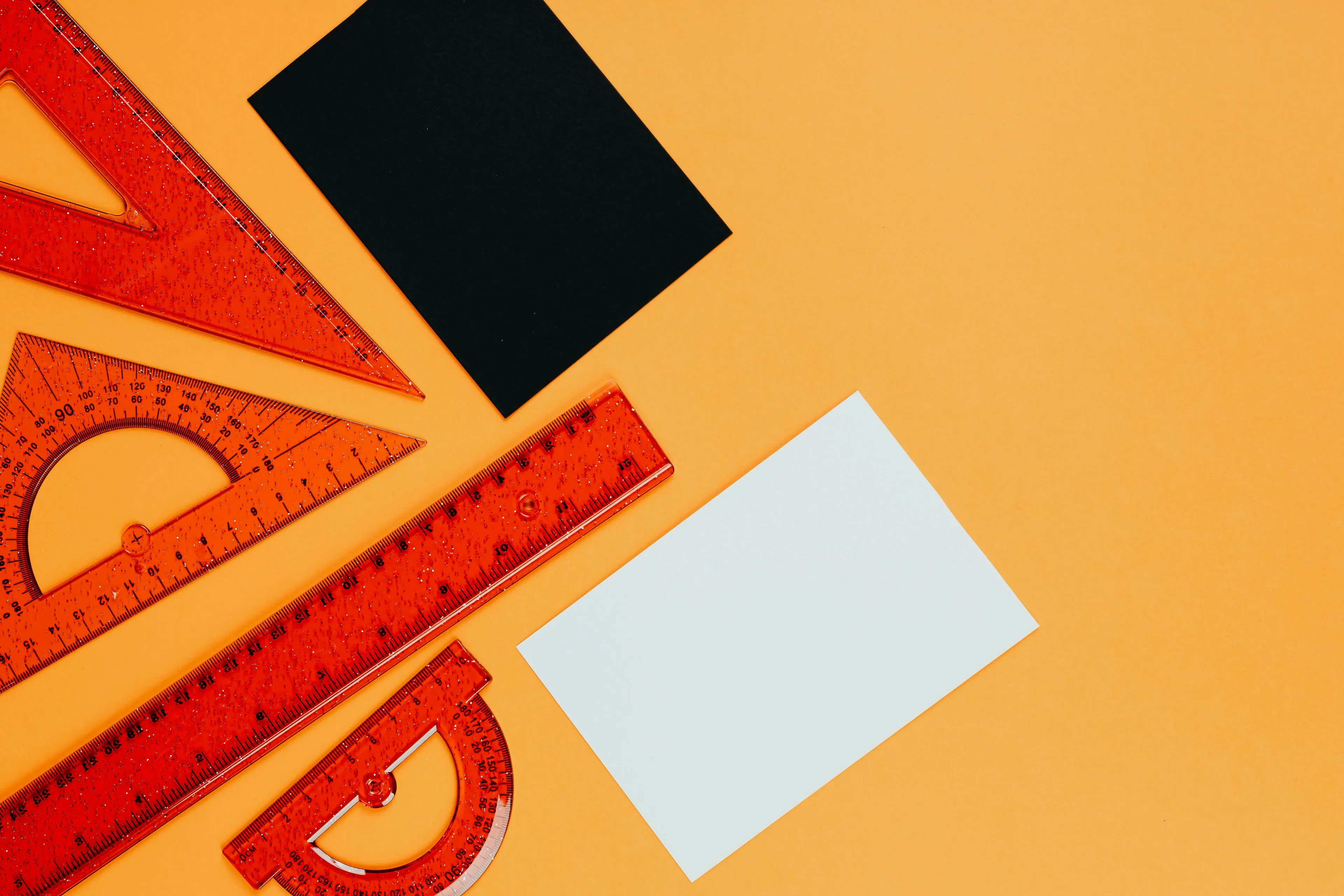 Red geometric rulers, protractors, and blank paper sheets on an orange background, related to geometry and knowledge.