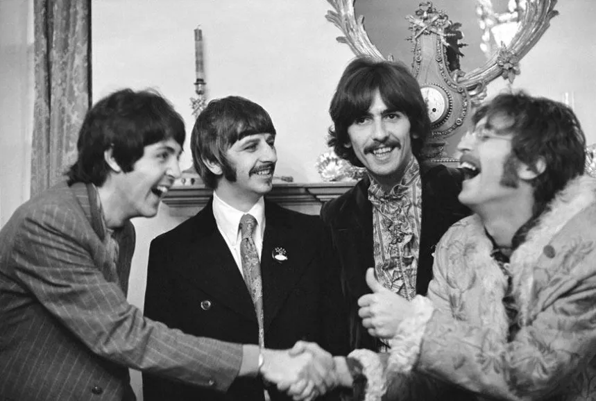 Black and white photo of The Beatles laughing and shaking hands. Test your General Knowledge quiz.