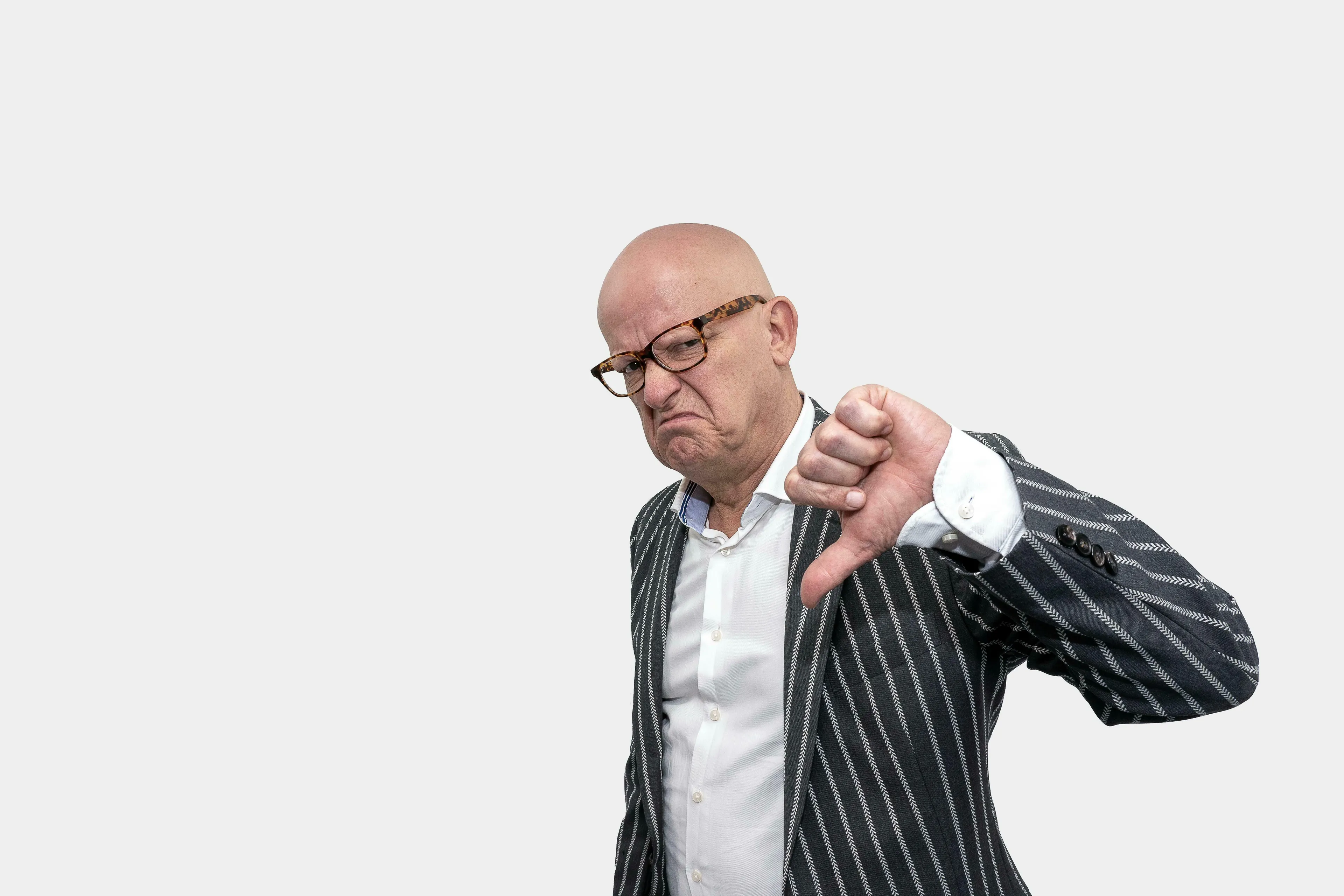 A man in glasses and a pinstripe jacket gives a thumbs-down, showing how harsh you are on yourself.