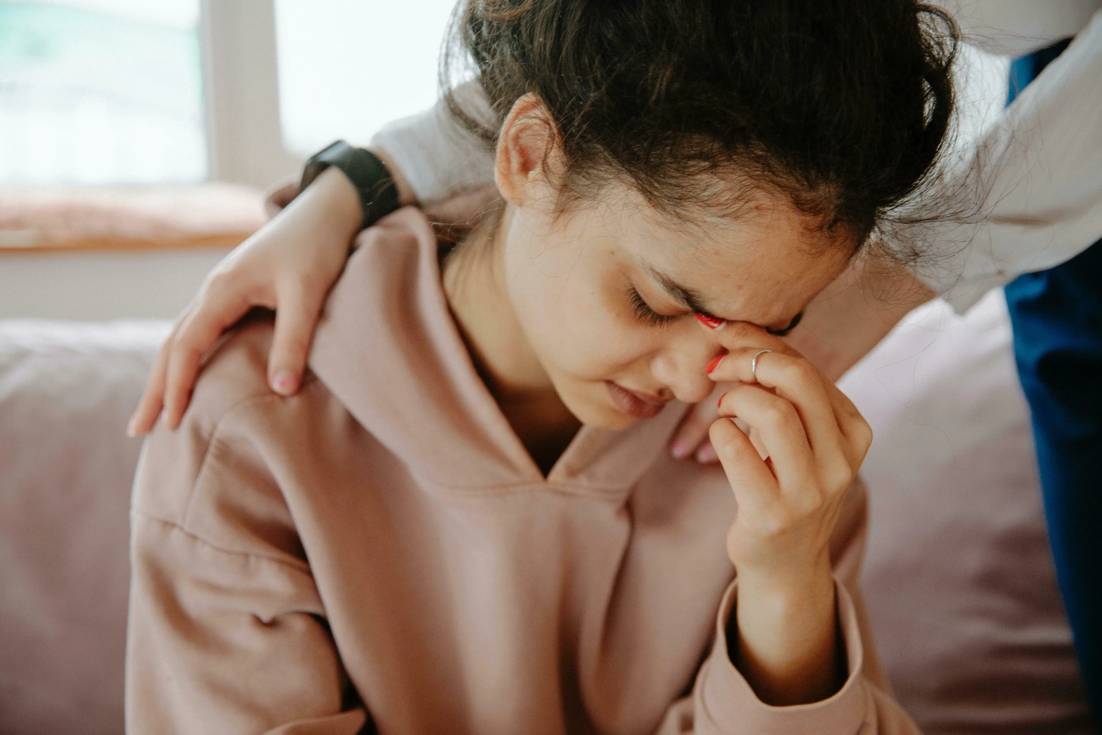 A young woman with closed eyes and a pained expression, being comforted by a hand on her shoulder. How harsh are you on yourself?
