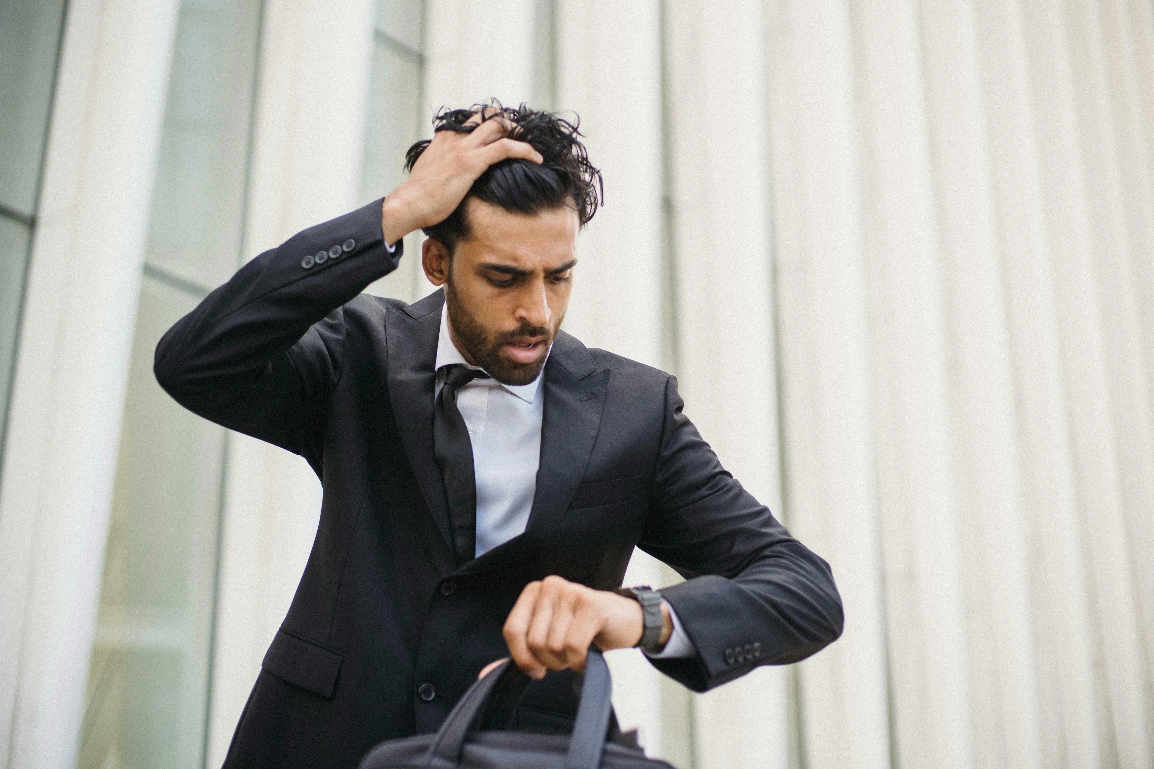 A man in a suit, hands in his hair, checks his watch, looking stressed. He's running late. How harsh are you on yourself?