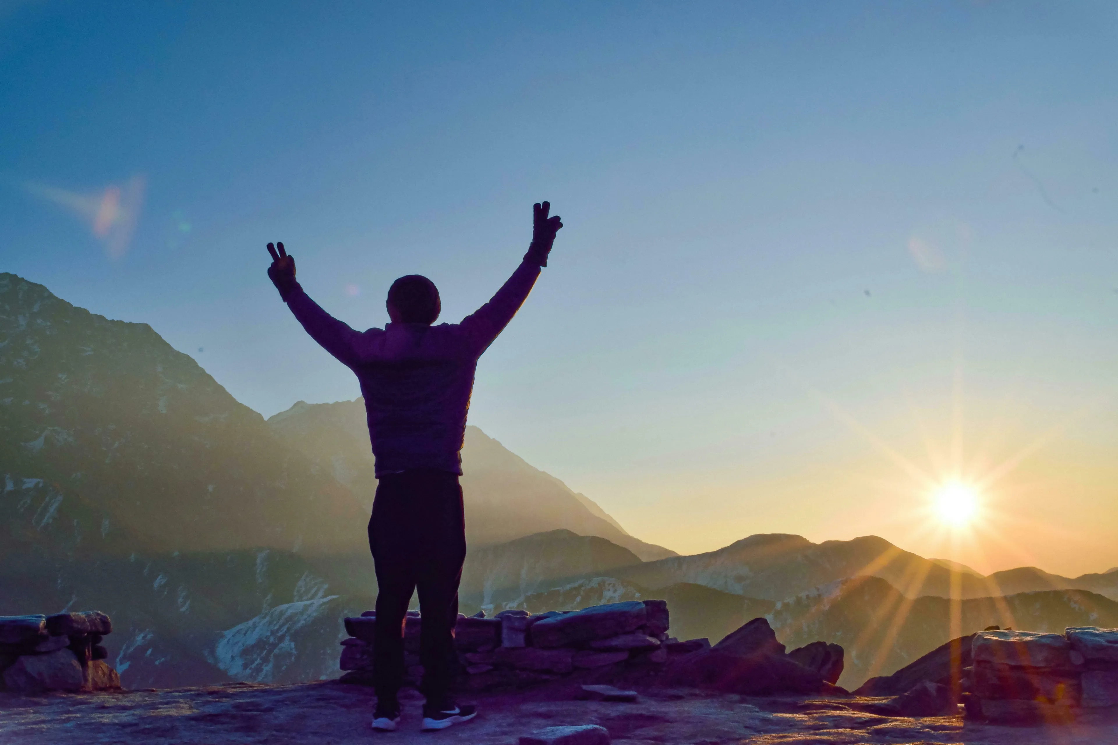 Silhouette of a person with arms raised in victory at sunset, celebrating an achievement on a mountain. How harsh are you on yourself?