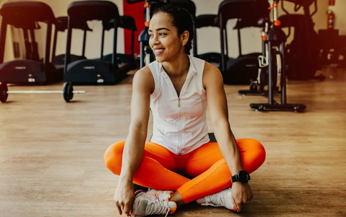 Smiling woman in activewear, sitting on gym floor. She just finished a workout and achieved her goal. General Knowledge Quiz.