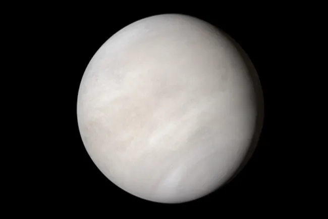 A pale, spherical Venus, a planet with swirling clouds, against the black expanse of space.