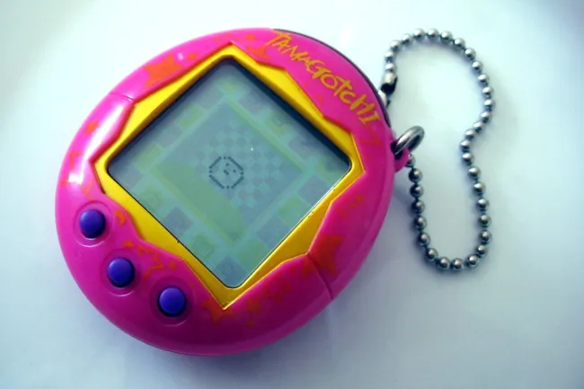 A pink Tamagotchi, a vintage virtual pet gadget, with purple buttons and a metal keychain, displaying a pixelated screen.
