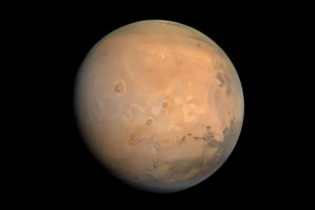 A full view of the planet Mars against a black background, showing its reddish-orange surface and varied terrain. Choose a planet.