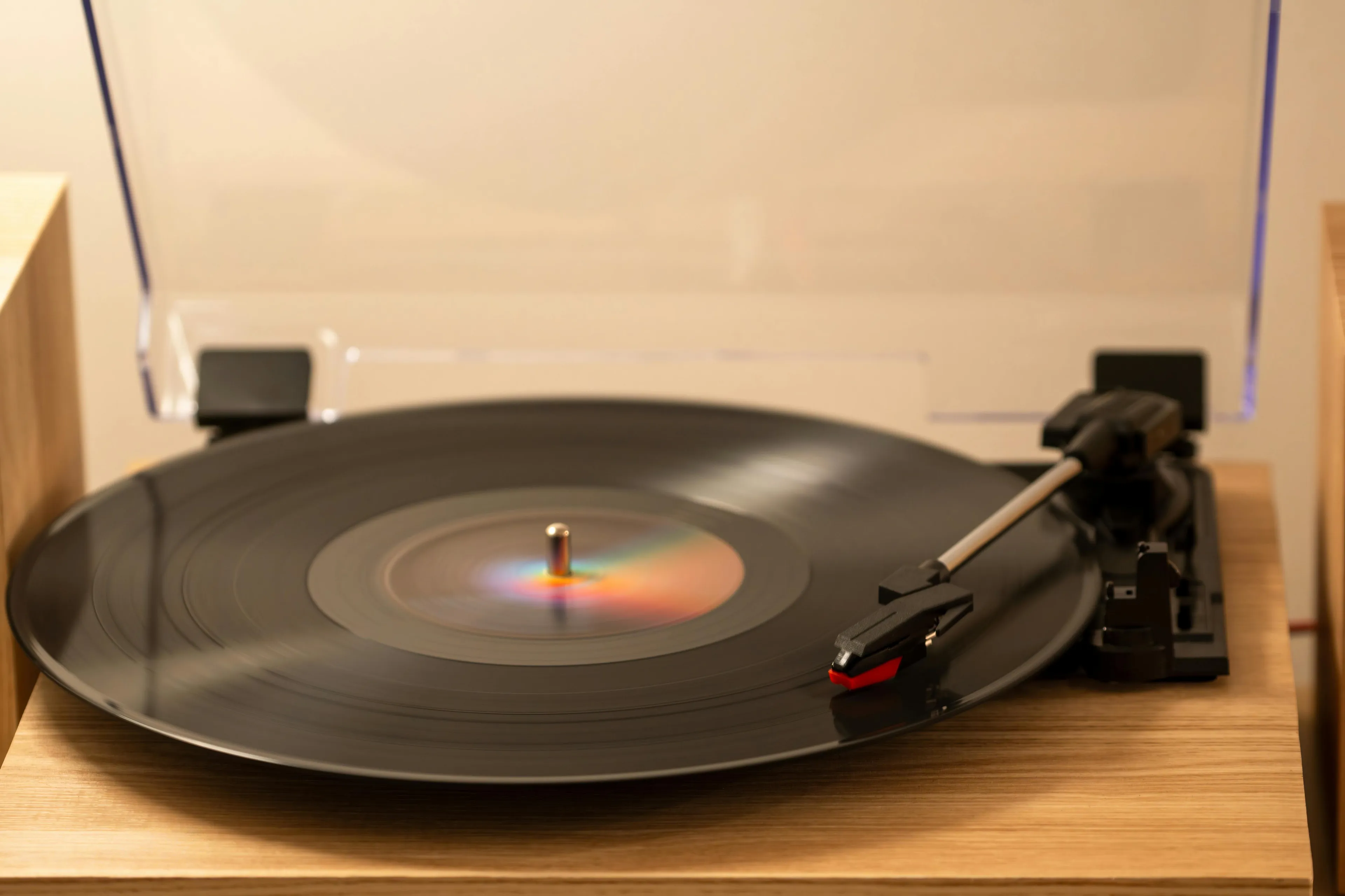 A vintage vinyl player with a black record spinning, showing a rainbow reflection from its center, on a wooden surface.