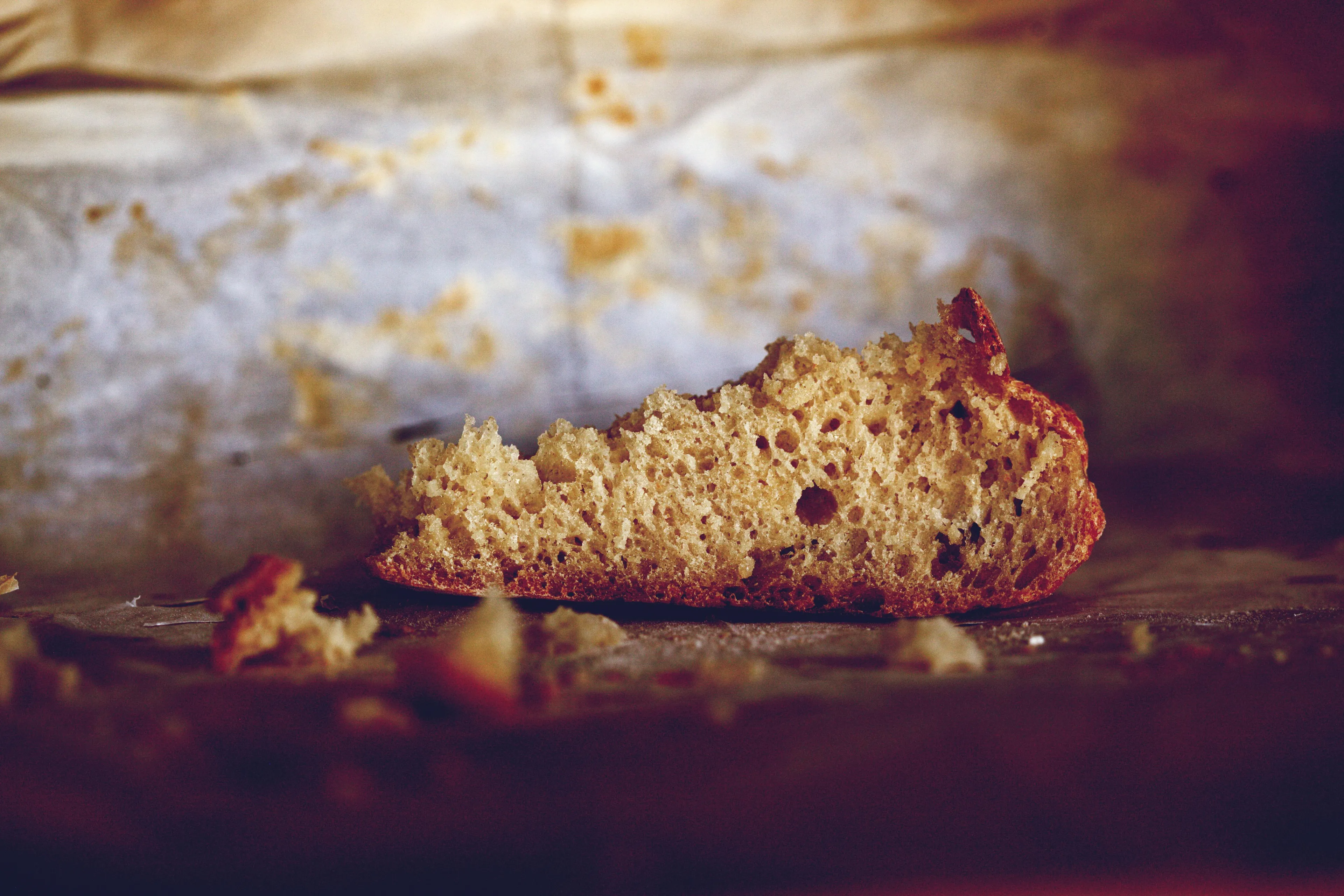 A torn piece of light brown bread, with a crusty base, on a blurry, textured background. A breakfast option.