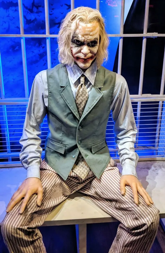 Wax figure of the Joker seated with iconic makeup and costume in a display