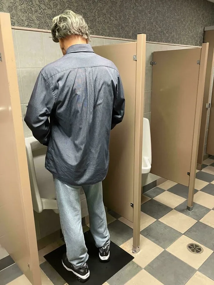 Back view of a celebrity wax figure standing at a urinal in a public restroom