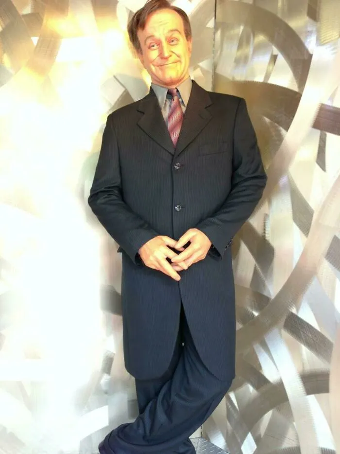 Smiling celebrity wax figure in a formal black suit with a purple tie