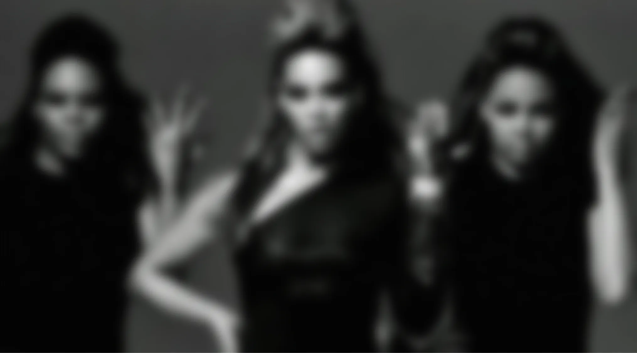 A blurry music video frame shows three women, possibly a girl group, in black clothing. Can you name the music video?
