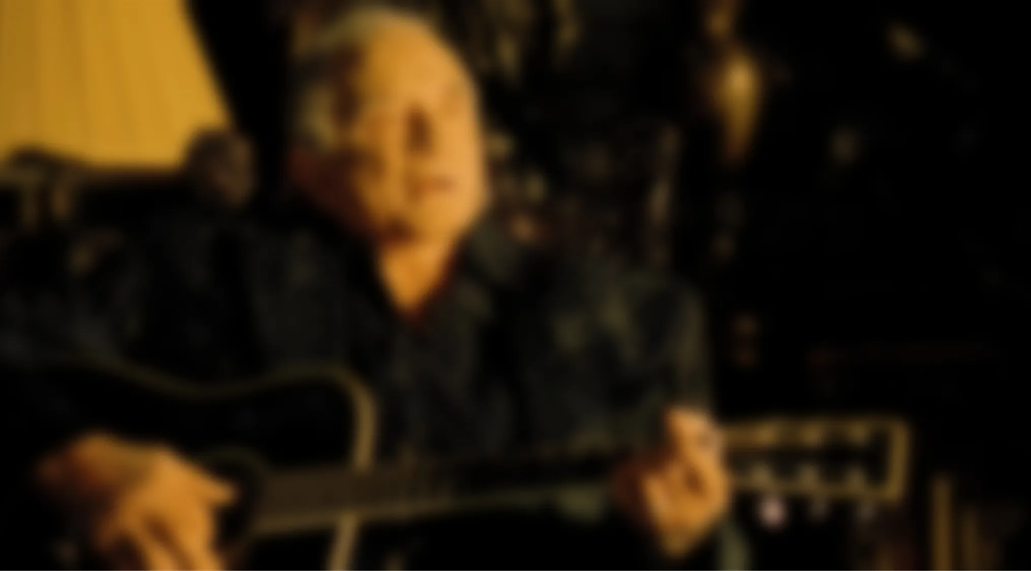 A blurry music video quiz image shows an older person playing a guitar in a dark setting, challenging viewers to recognize the video behind the blur.
