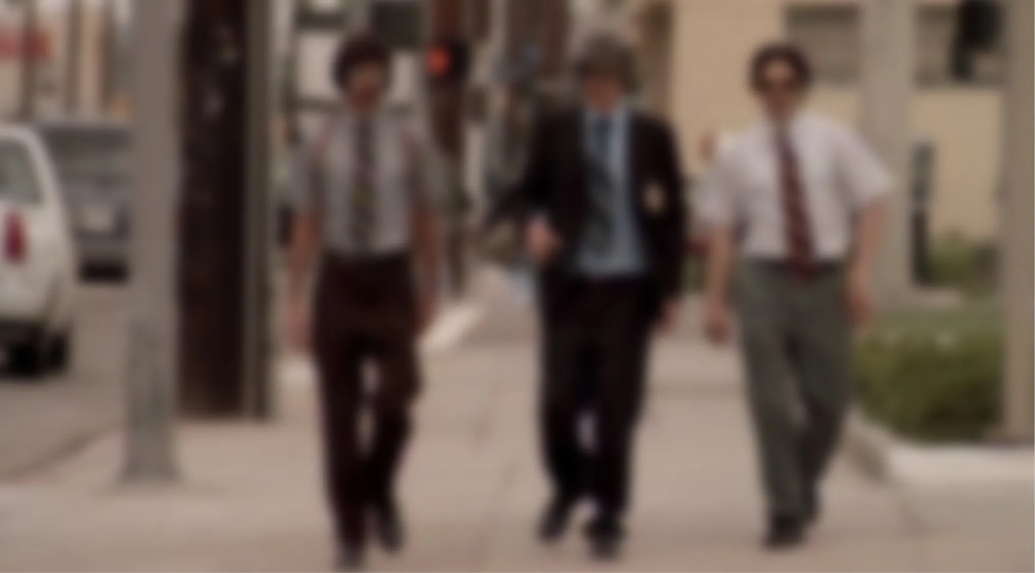 A blurry music video image showing three men in suits walking on a sidewalk. Blurry music videos quiz.