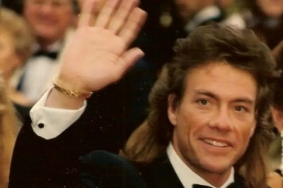 Jean-Claude Van Damme, bodybuilder-turned-actor, waves with a big smile, wearing a tuxedo.